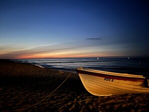 Un bateau nommé « KOS 6 » est échoué sur une plage au crépuscule.