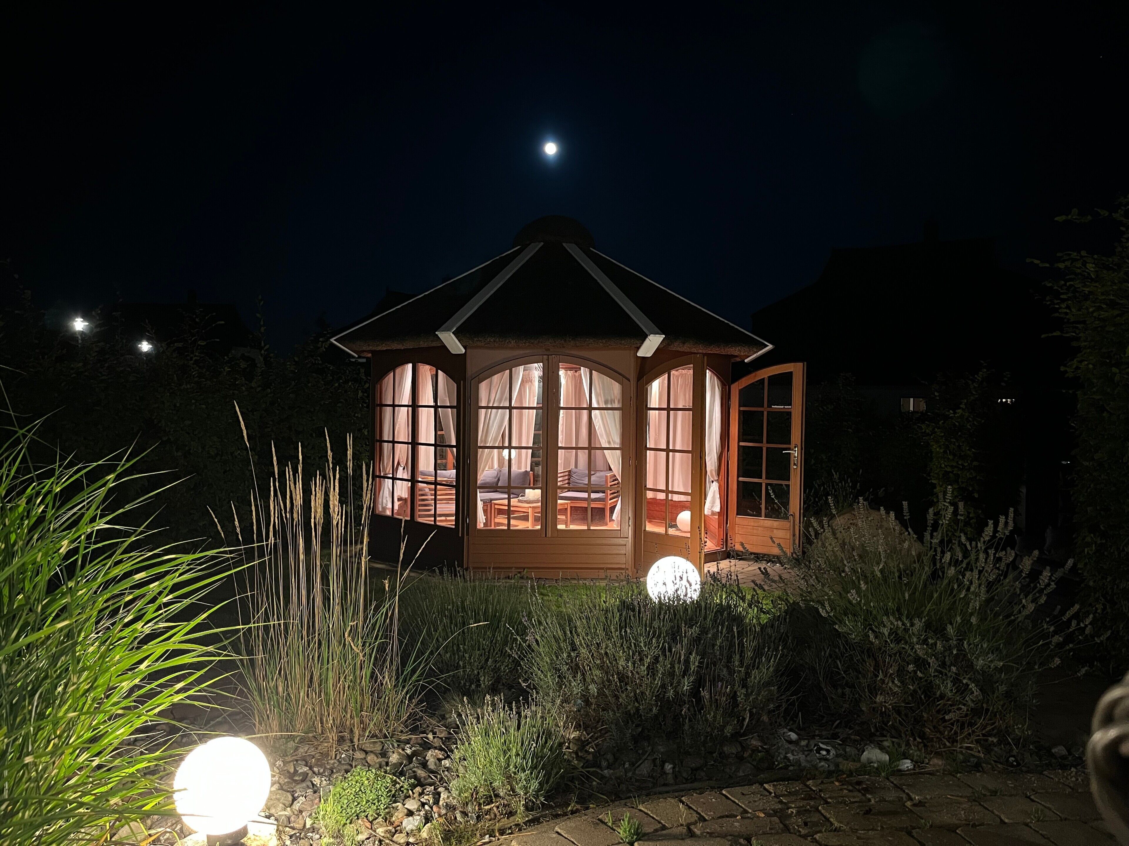 A wooden gazebo with a thatched roof, large windows, and a door.