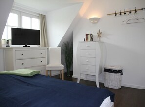 A bedroom with a bed, a dresser, a chair, a television, a wall-mounted light, and a small plant. - Holiday Home 'Villa Sorgenfrei' with Lake View, Private Terrace and Wi-Fi (Zinnowitz)