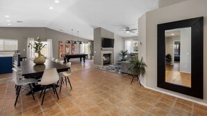 A spacious living area with a fireplace, a dining table with chairs, and a TV mounted on the wall. - Desert Paradise - Arcade, Casino, Spa, Play Area, Water Slide, Pool Table (Indio)