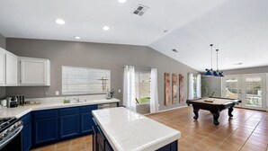 A spacious kitchen with blue cabinets, a white island, and a pool table. - Desert Paradise - Arcade, Casino, Spa, Play Area, Water Slide, Pool Table (Indio)
