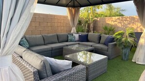 A covered outdoor seating area with a sectional sofa and a glass coffee table. - Desert Paradise - Arcade, Casino, Spa, Play Area, Water Slide, Pool Table (Indio)