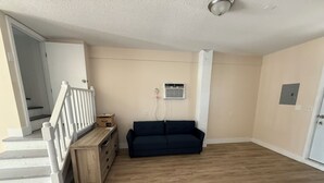 A spacious living room with a dark blue sofa, wooden flooring, a staircase with white railings, and a white door.