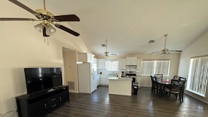 A spacious living area with a TV, black entertainment unit, and a dining table with chairs.