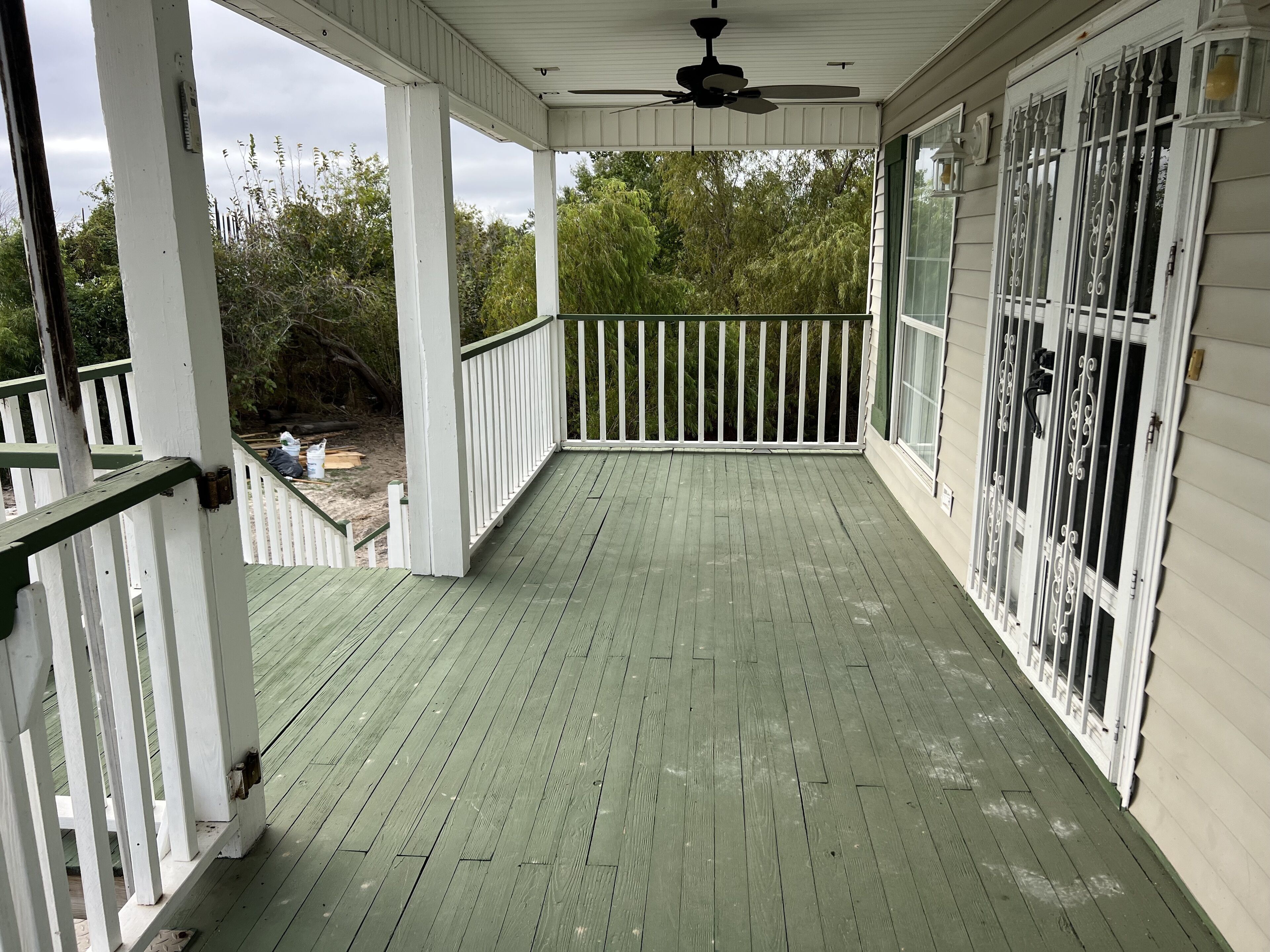 Une véranda couverte avec un plancher en bois vert, des balustrades blanches et un ventilateur de plafond.