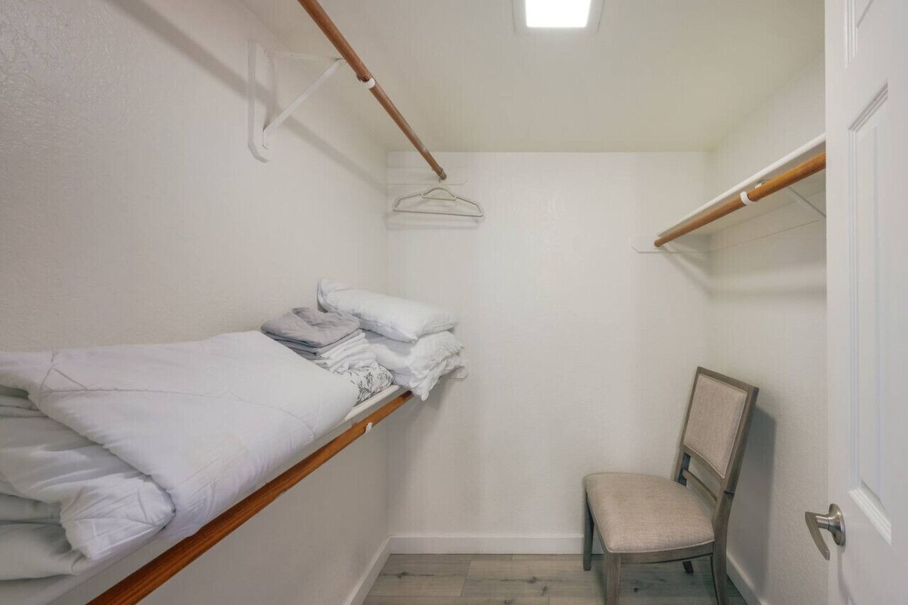 Ein kleines Zimmer mit einem Einzelbett, Holzrahmen, einem Stuhl und einer Kleiderstange.
