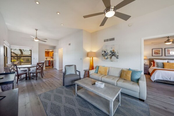 A spacious living area with a dining table, sofa, and coffee table. There is a ceiling fan and a painting on the wall.