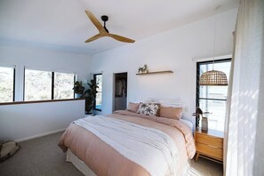 A bedroom with a bed, a ceiling fan, a window, and a shelf with decorative items.