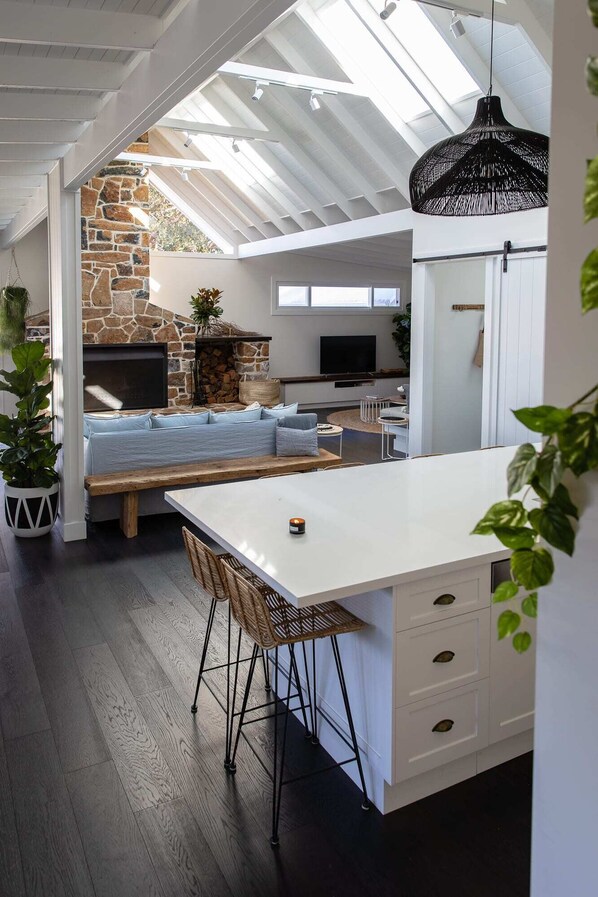 A modern kitchen with a large island, stone fireplace, and a skylight.