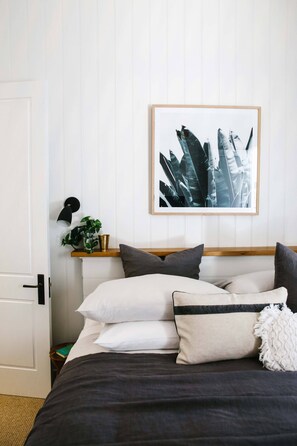 A neatly made bed with a dark bedspread, multiple pillows, and a framed artwork above it.
