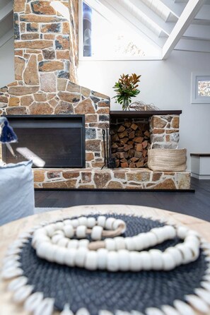 A stone fireplace with a flat-screen TV, a log fire, and a decorative plant. - Soul of Gerringong Farmhouse (Gerringong)