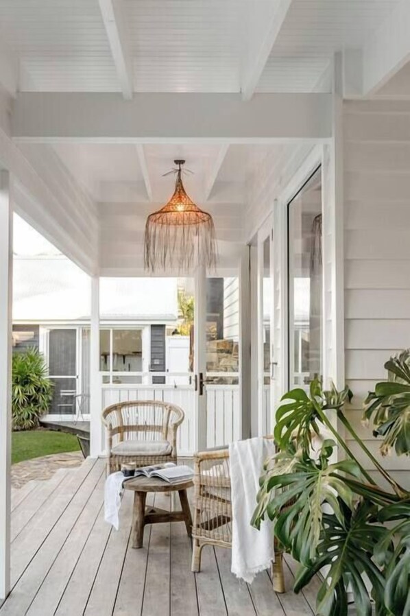 A covered porch with wicker chairs, a hanging light fixture, and potted plants.