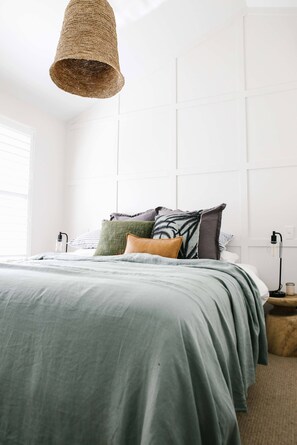 A bedroom with a bed, pillows, a hanging light fixture, and a bedside table.