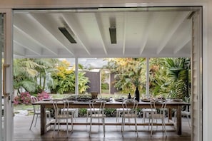 Comedor de concepto abierto con una larga mesa y sillas, rodeado de exuberante follaje.