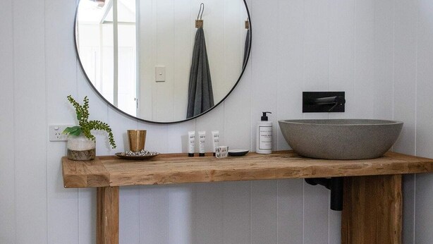 Un baño con tocador de madera, espejo redondo, lavabo sobre encimera y suelo con patrón hexagonal.