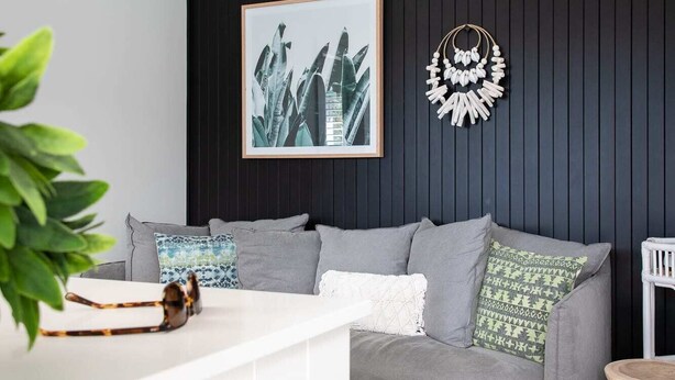 Een moderne woonkamer met een grijze bank, een ingelijste botanische print en een decoratief wandobject.