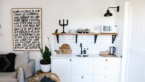 Een kleine keuken met witte kastjes, een houten aanrecht, een spoelbak en een zwarte hanglamp.