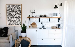 A compact kitchen with white cabinetry, a wooden countertop, a sink, a microwave, and a black pendant light.