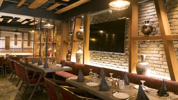 Un restaurante con mesas largas compartidas, asientos tipo banca tapizados en rojo y un fondo de pared de ladrillo.