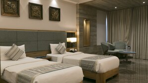 Habitación de hotel con dos camas, un escritorio, una silla y una mesita. Hay lámparas fijadas a la pared y cuadros enmarcados.