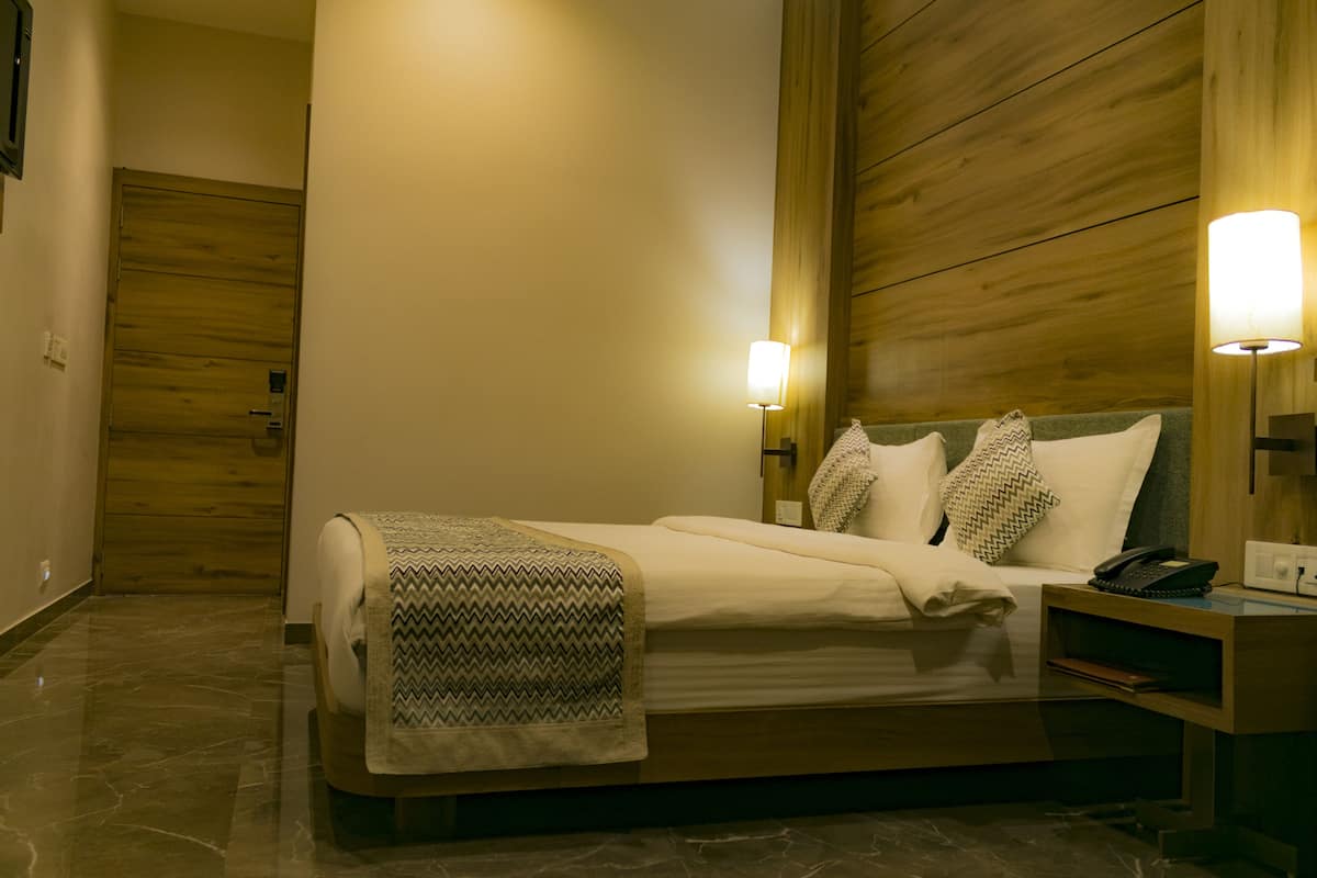 A modern hotel room with a wooden headboard, a bed with a patterned throw, two bedside lamps, and a bedside table with a phone.