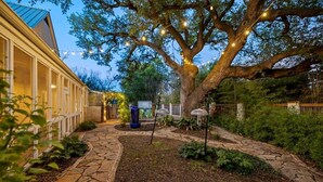 Un camino de piedra que conduce a una casa con un gran árbol y luces colgantes.