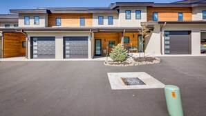 A modern multi-story building with multiple garage doors, a small landscaped area with a tree, and a storm drain. - Angel Fire Home w/ Hot Tub < 1 Mi to Ski Slopes! (Angel Fire)
