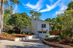A two-story house with a stone chimney, a garage, and a landscaped front yard with trees and shrubs.