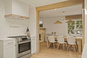 A modern kitchen with a built-in oven, a dining area with a wooden table and chairs, and a view through an open doorway.