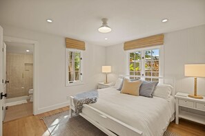 A bedroom with a bed, bedside tables, lamps, a window with blinds, and a door leading to a bathroom.