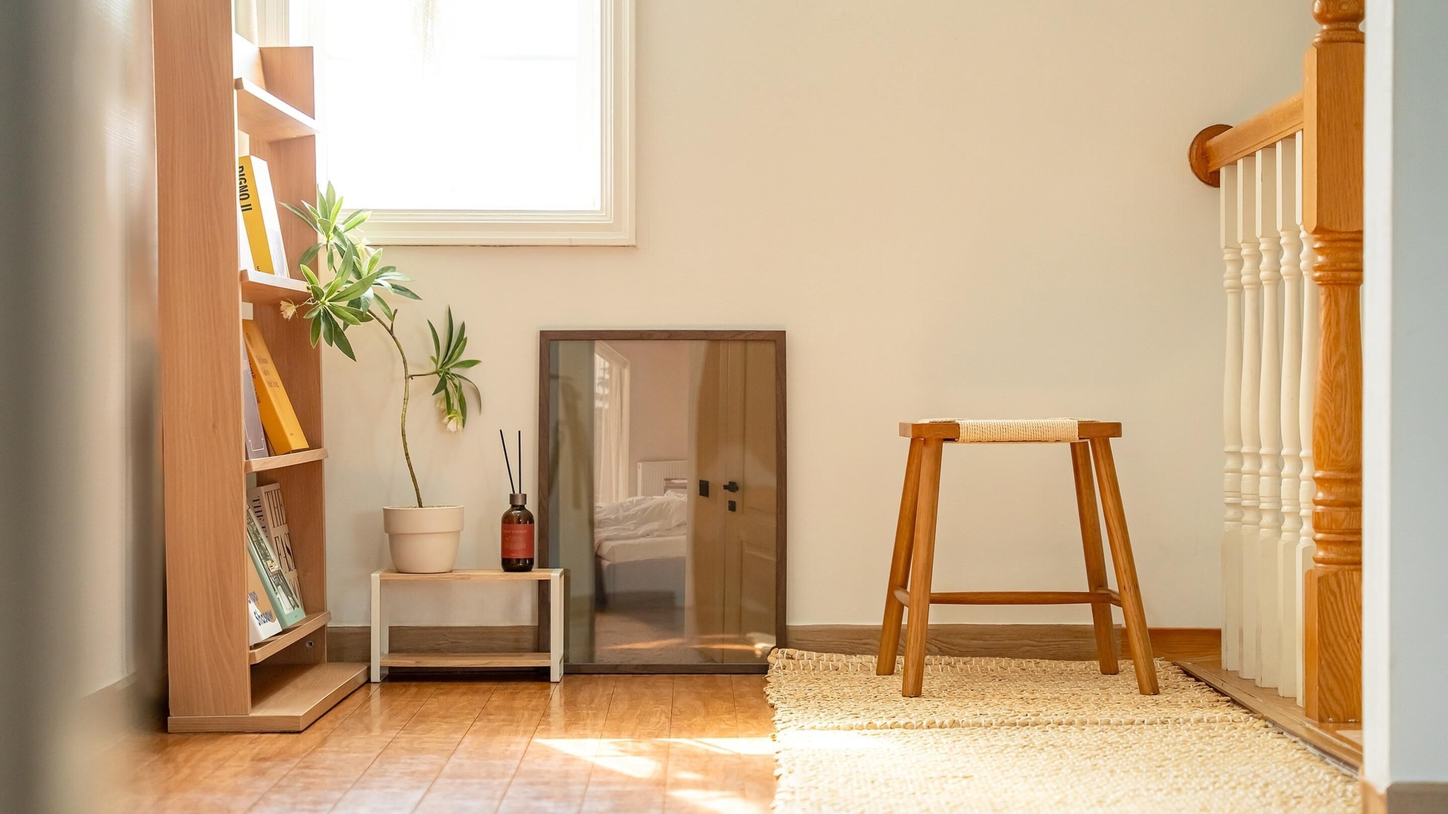Una habitación con una estantería de madera, una planta en maceta, un taburete pequeño y una puerta que da a otra habitación.