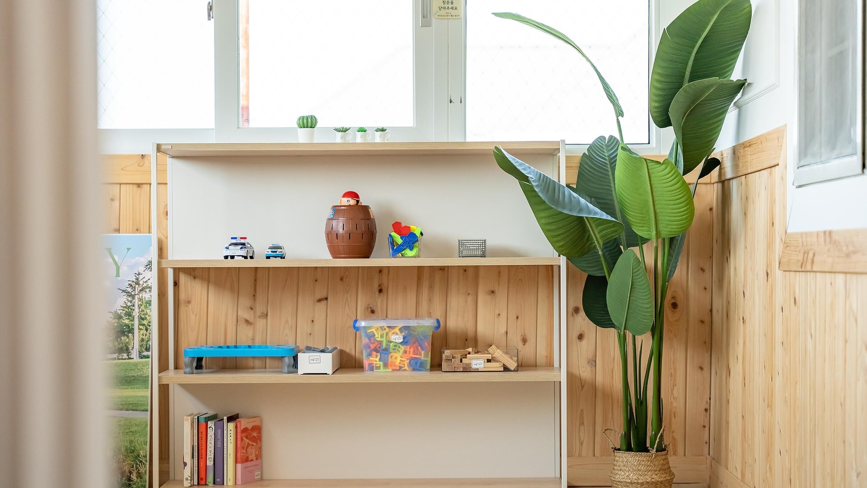 Una estantería de madera con juguetes, libros y una planta.