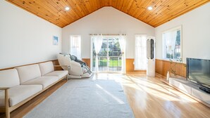 Ein geräumiges Wohnzimmer mit hohen Holzbalken, einem großen Fenster, einem Massagesessel, einem Flachbildfernseher und einem Holzboden.