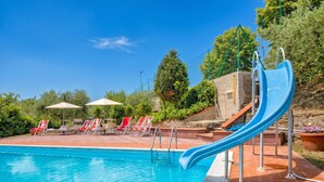 Ein Swimmingpool mit einer blauen Rutsche, roten Liegestühlen und Sonnenschirmen.