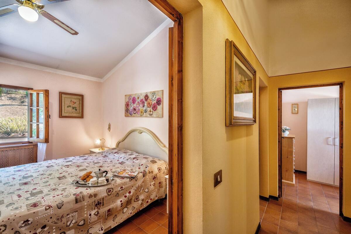 A bedroom with a bed, a window, a ceiling fan, and a door leading to another room.
