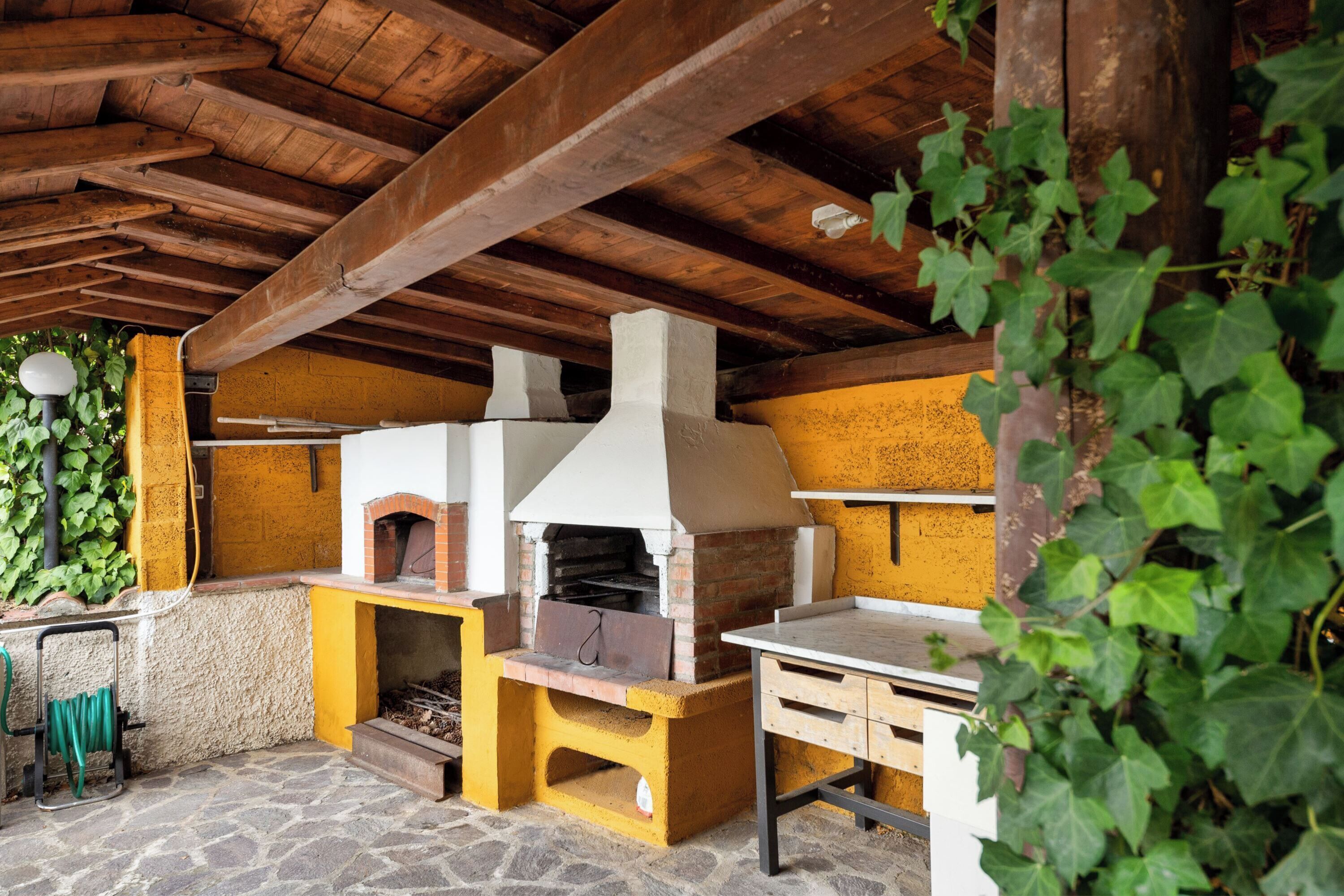 An outdoor kitchen area with a brick oven, stone flooring, and wooden beams.