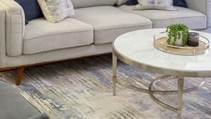 Una sala de estar con un sofá gris, una mesa redonda de centro y un tapete estampado.