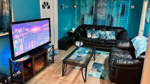 A living room with teal walls, a black leather sofa, a glass coffee table, and a flat-screen TV. - This special place is close to everything, making it easy to plan your visit.  (Smyrna)