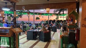 A restaurant with outdoor seating, a wooden interior, and a view of the sea at sunset. - Mountain Top Park Hotel (Quepos)