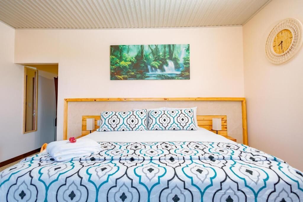 A hotel room with a bed, a painting of a waterfall, a clock, and a wooden headboard.