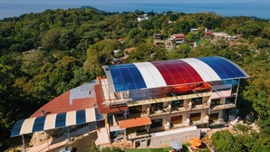 A modern building with a large, curved roof, surrounded by lush greenery and a view of the sea. - Mountain Top Park Hotel (Quepos)