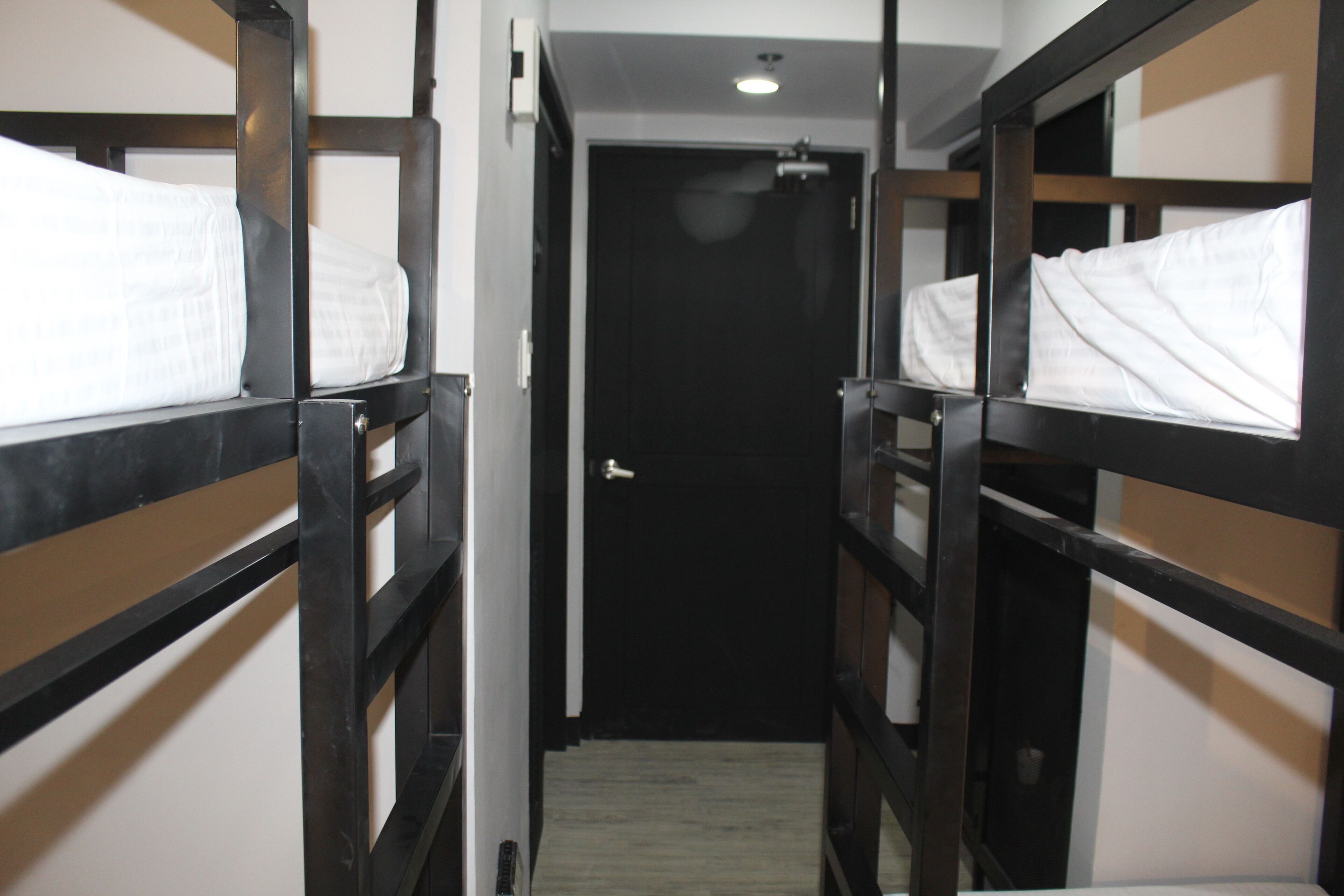 A narrow corridor with bunk beds on either side, leading to a dark door at the end.