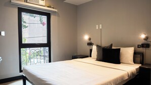 A neatly made bed with white linens, a window with a view of greenery, and two bedside lamps. - Mad Monkey Manila (Makati)