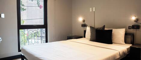 Una cama bien hecha con ropa de cama blanca, una ventana con vistas a la vegetación y dos lámparas de noche.