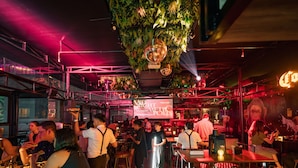 A bustling indoor venue with tables and chairs, a stage with a large screen, and decorative plants. - Mad Monkey Manila (Makati)