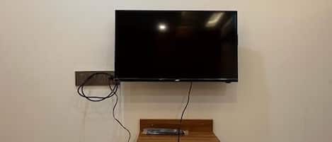 Ein Flachbildfernseher an der Wand befestigt, darunter ein Holzregal.