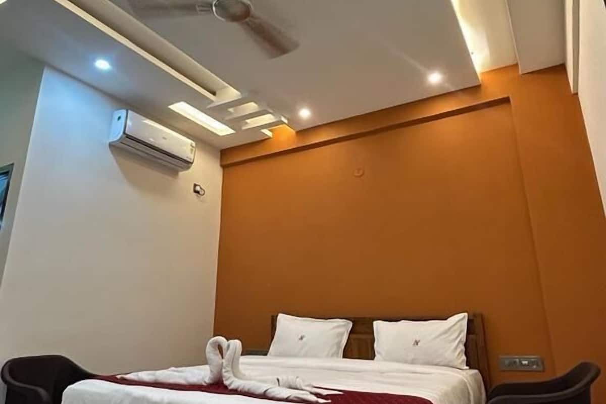Quarto moderno com cama de madeira, roupa de cama branca, ventoinha no teto, iluminação embutida e unidade de ar condicionado.