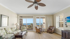 A spacious living room with a ceiling fan, a sofa, two armchairs, a coffee table, and a TV. Large windows offer a view of the sea. - Reflections at Bay Point Unit 412 (Panama City Beach)