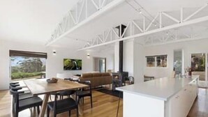 A modern kitchen with a central island, a dining area with a wooden table and chairs, and a large window offering a view of greenery. - NewHaven, private retreat overlooking Dover Bay (Dover)