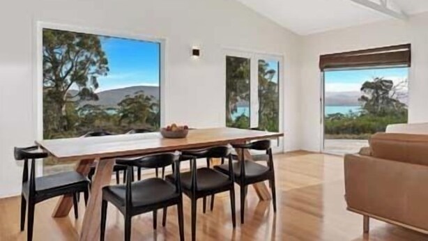A modern dining area with a wooden table and chairs, large windows with scenic views, and a brown sofa. - NewHaven, private retreat overlooking Dover Bay (Dover)